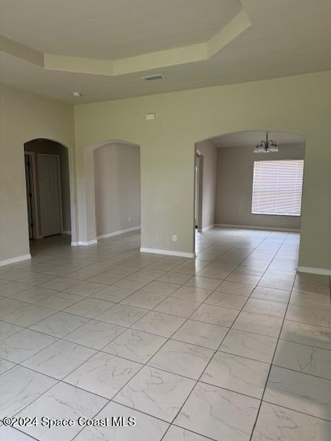 unfurnished room featuring a tray ceiling and an inviting chandelier