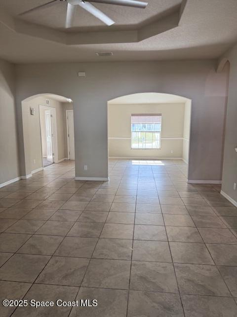 tiled empty room with a tray ceiling, a high ceiling, and ceiling fan