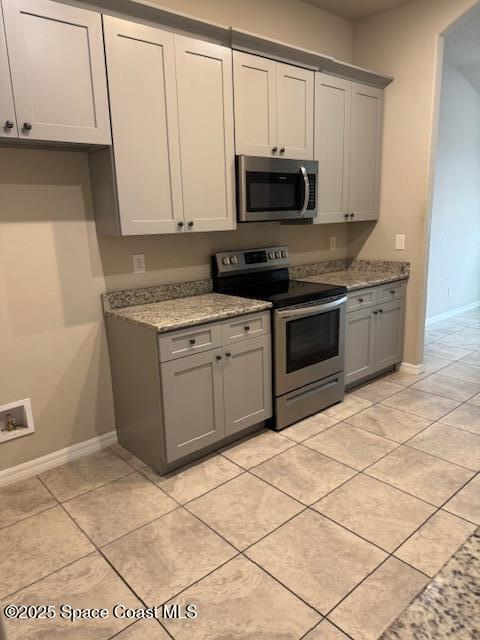 kitchen with appliances with stainless steel finishes, gray cabinets, light tile patterned floors, and light stone counters