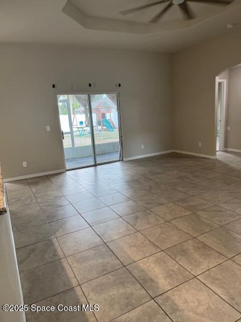 empty room with a tray ceiling, ceiling fan, and light tile patterned floors