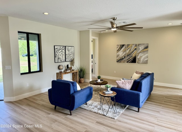 living room featuring ceiling fan, a textured ceiling, and light hardwood / wood-style flooring