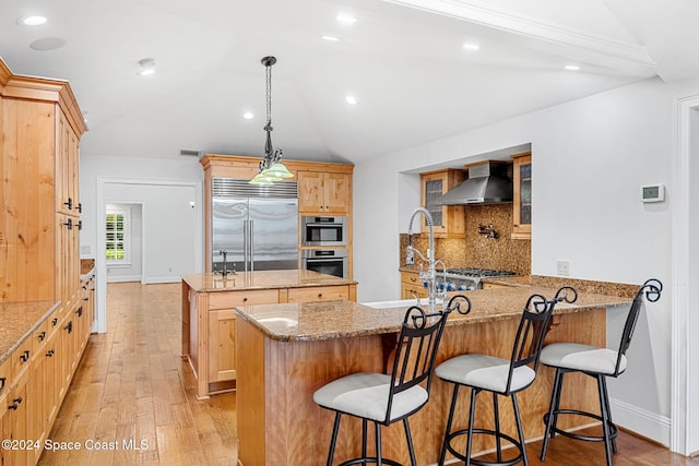 kitchen with lofted ceiling, light hardwood / wood-style flooring, wall chimney exhaust hood, kitchen peninsula, and stainless steel appliances