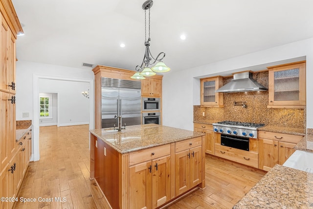 kitchen featuring a kitchen island with sink, light hardwood / wood-style flooring, wall chimney range hood, and appliances with stainless steel finishes