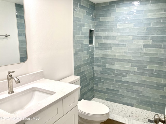 bathroom with a tile shower, vanity, and toilet