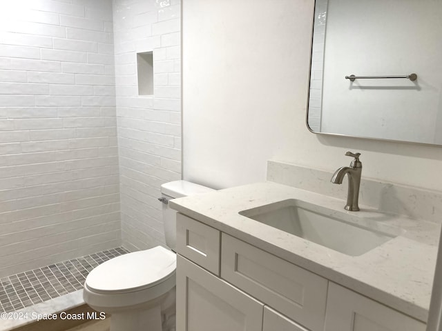 bathroom with toilet, a tile shower, and vanity