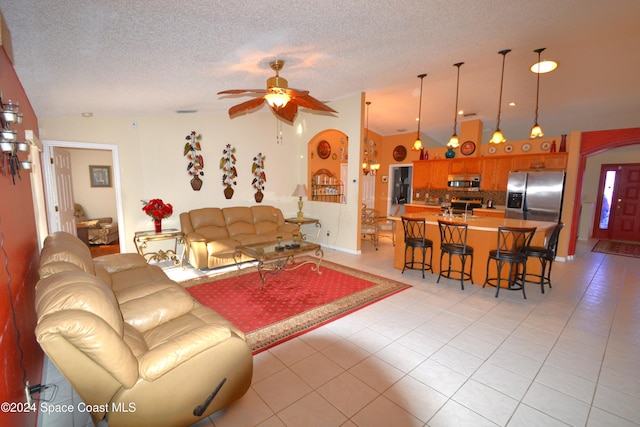 living room with ceiling fan, light tile patterned floors, a textured ceiling, and vaulted ceiling