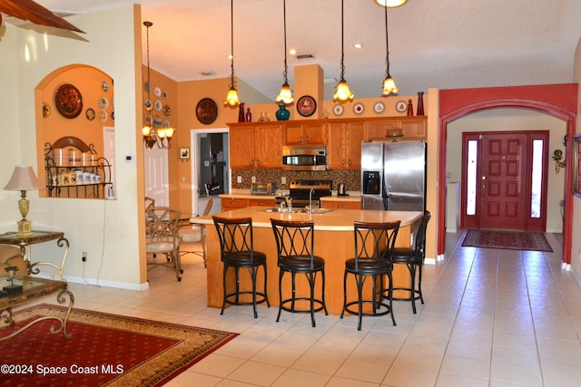 kitchen with appliances with stainless steel finishes, a kitchen breakfast bar, sink, high vaulted ceiling, and hanging light fixtures