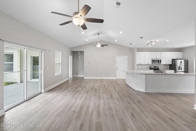 kitchen with backsplash, vaulted ceiling, light wood-type flooring, appliances with stainless steel finishes, and white cabinetry