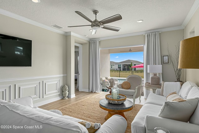 living room featuring crown molding, light hardwood / wood-style flooring, ceiling fan, and a textured ceiling