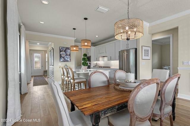 dining area with a textured ceiling, an inviting chandelier, light hardwood / wood-style flooring, and ornamental molding