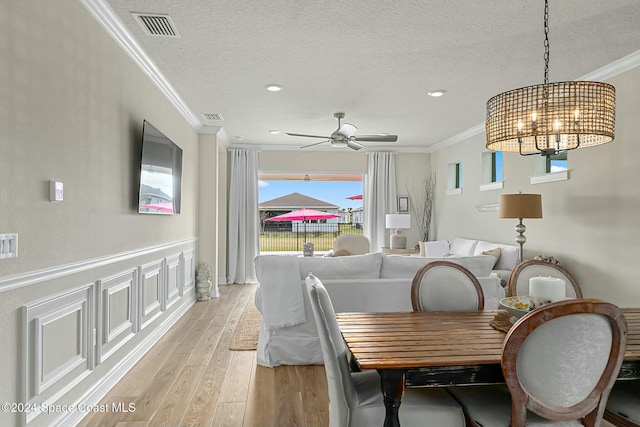 dining area featuring a textured ceiling, ceiling fan with notable chandelier, light hardwood / wood-style flooring, and crown molding