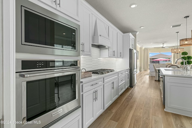 kitchen with sink, hanging light fixtures, light hardwood / wood-style flooring, white cabinetry, and stainless steel appliances