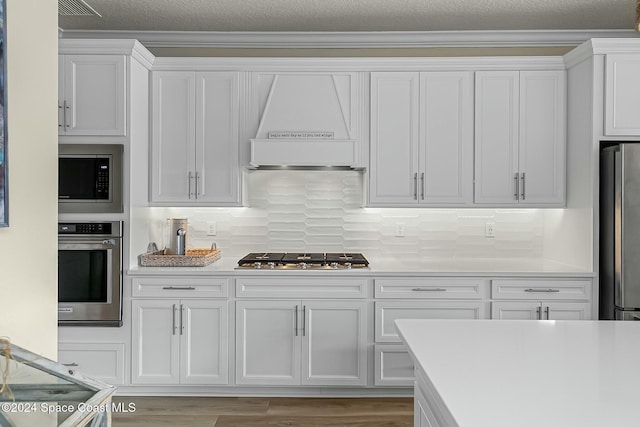 kitchen with white cabinets, appliances with stainless steel finishes, light hardwood / wood-style floors, and custom exhaust hood