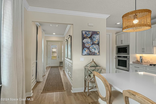 kitchen with ornamental molding, stainless steel appliances, light hardwood / wood-style floors, white cabinetry, and hanging light fixtures