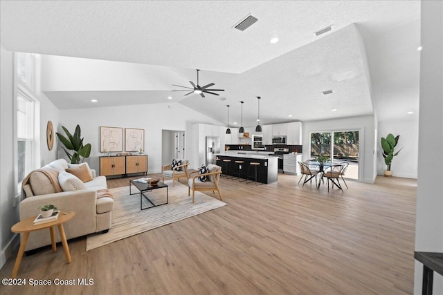 living room featuring a textured ceiling, light wood-type flooring, vaulted ceiling, and ceiling fan