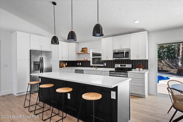 kitchen featuring pendant lighting, backsplash, light hardwood / wood-style flooring, appliances with stainless steel finishes, and white cabinetry