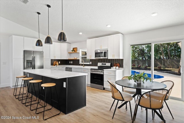 kitchen featuring decorative light fixtures, stainless steel appliances, white cabinetry, and a kitchen island