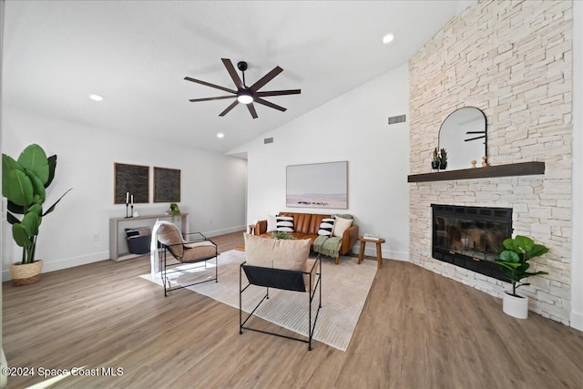 living room featuring wood-type flooring, high vaulted ceiling, a stone fireplace, and ceiling fan