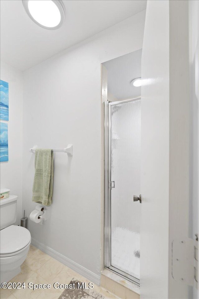 bathroom featuring toilet, tile patterned floors, and a shower with shower door