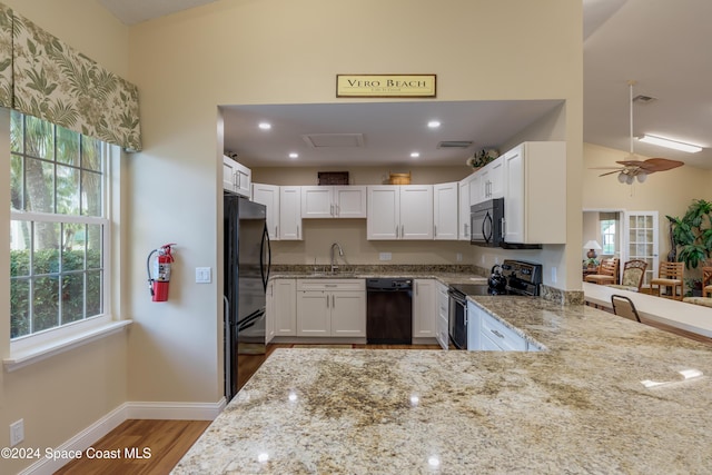 kitchen with kitchen peninsula, light stone countertops, a healthy amount of sunlight, and black appliances