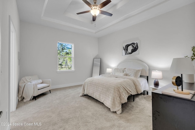 bedroom with light colored carpet, ceiling fan, and a tray ceiling