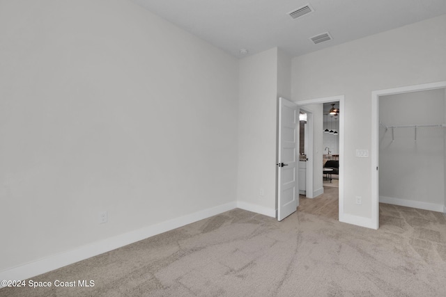 unfurnished bedroom featuring a walk in closet, a closet, and light colored carpet