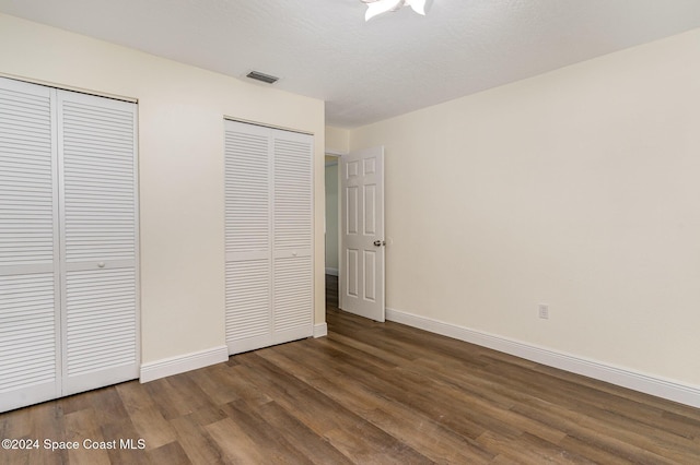 unfurnished bedroom featuring a textured ceiling, dark hardwood / wood-style flooring, and multiple closets