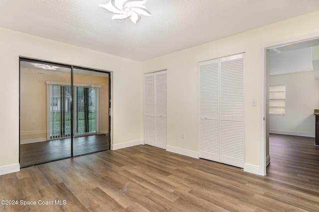 unfurnished bedroom featuring access to exterior, hardwood / wood-style floors, a textured ceiling, and multiple closets