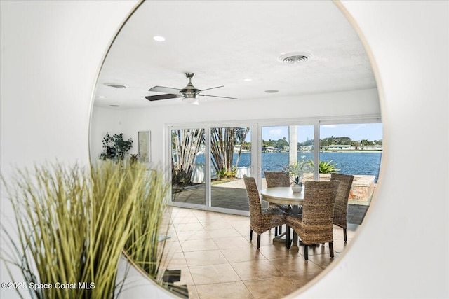 tiled dining space with ceiling fan and a water view