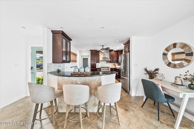 kitchen featuring kitchen peninsula, ceiling fan, stainless steel appliances, decorative backsplash, and wall chimney exhaust hood