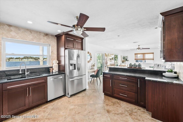 kitchen with ceiling fan, sink, appliances with stainless steel finishes, a water view, and dark stone counters