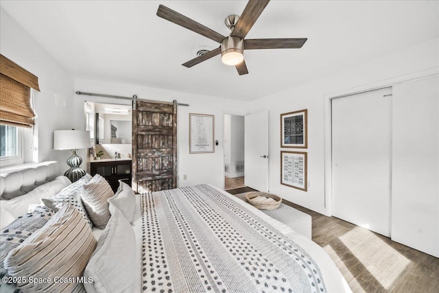 bedroom with ceiling fan, a barn door, a closet, and dark hardwood / wood-style floors