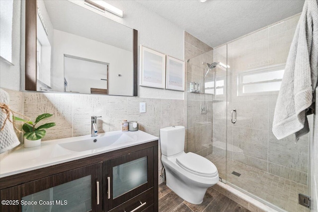 bathroom with a textured ceiling, vanity, tile walls, toilet, and a shower with shower door