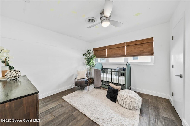 bedroom featuring ceiling fan, dark wood-type flooring, and a crib