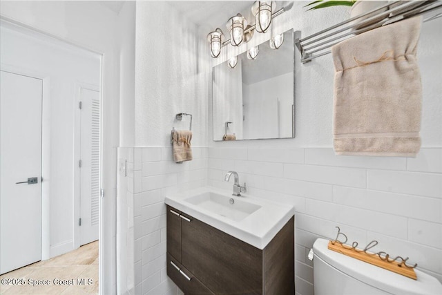 bathroom with toilet, tile patterned flooring, tile walls, and vanity