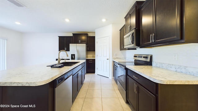 kitchen featuring a center island with sink, sink, light tile patterned floors, a textured ceiling, and appliances with stainless steel finishes