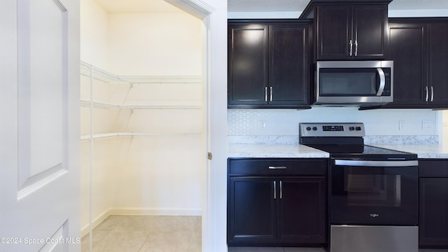 kitchen with backsplash, dark brown cabinetry, light tile patterned floors, and stainless steel appliances