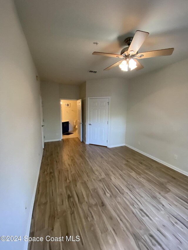 unfurnished bedroom with wood-type flooring, a closet, ensuite bath, and ceiling fan