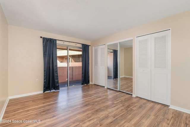 unfurnished bedroom featuring hardwood / wood-style floors and two closets