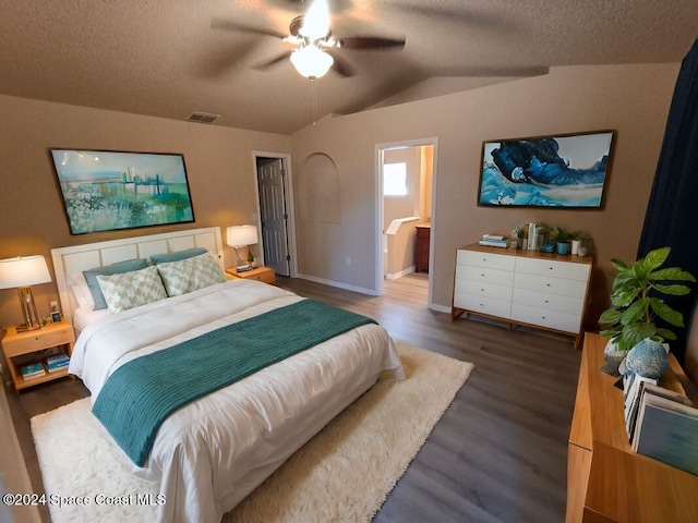 bedroom with ensuite bath, a textured ceiling, vaulted ceiling, ceiling fan, and dark wood-type flooring