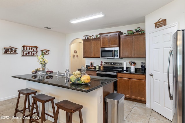 kitchen with sink, stainless steel appliances, a kitchen bar, a center island with sink, and light tile patterned floors