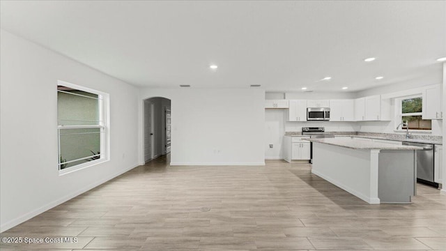 kitchen featuring a kitchen island, appliances with stainless steel finishes, white cabinetry, sink, and light stone countertops