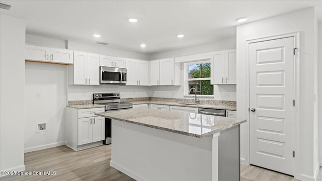 kitchen featuring sink, light stone counters, a center island, appliances with stainless steel finishes, and white cabinets