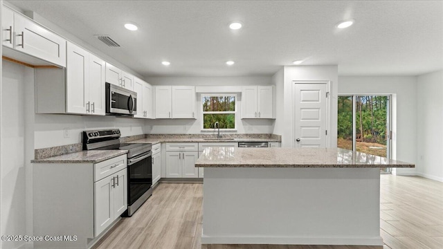 kitchen with white cabinetry, stainless steel appliances, light stone countertops, and a kitchen island