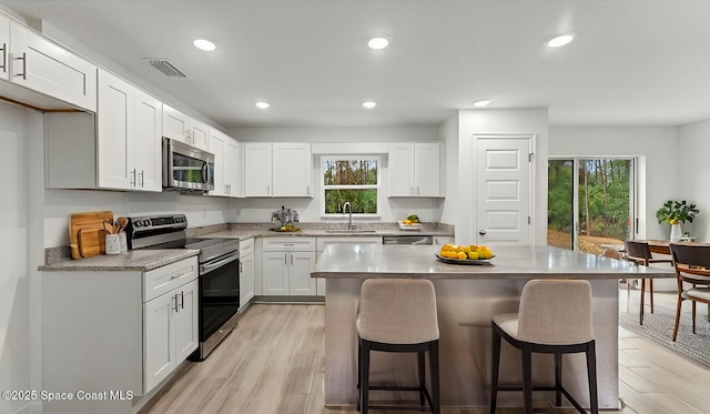 kitchen with appliances with stainless steel finishes, a kitchen breakfast bar, sink, and white cabinets