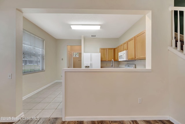 kitchen featuring kitchen peninsula, white appliances, light brown cabinetry, and light tile patterned floors