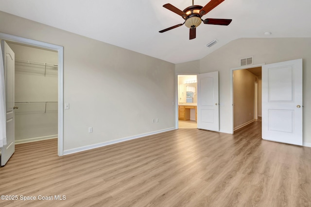 unfurnished bedroom with a spacious closet, vaulted ceiling, a closet, light hardwood / wood-style flooring, and ceiling fan