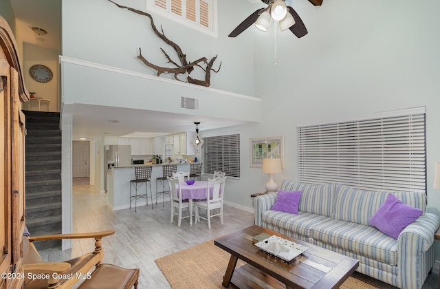 living room with ceiling fan, light hardwood / wood-style flooring, and a towering ceiling