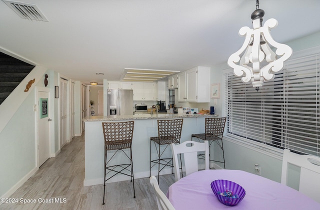 kitchen with pendant lighting, light hardwood / wood-style flooring, stainless steel fridge with ice dispenser, light stone counters, and white cabinetry