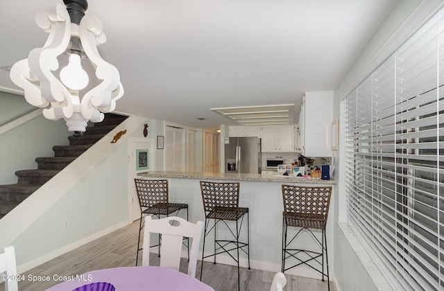 kitchen with stainless steel fridge, light wood-type flooring, a kitchen breakfast bar, an inviting chandelier, and white cabinets